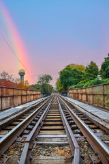 Fototapeta na wymiar as long set of rusty iron and wood railroad tracks surrounded by the Sunsphere and autumn colored trees and lush green trees with powerful clouds and a rainbow at World's Fair Park