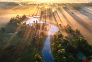 Luftaufnahme des schönen geschwungenen Flusses im Nebel bei Sonnenaufgang im Herbst in der Ukraine. Flussschleifen, Wiesen, Orangengras, neblige Bäume, goldene Sonnenstrahlen in der Morgendämmerung im Herbst. Bunte Luftlandschaft. Ansicht von oben © den-belitsky