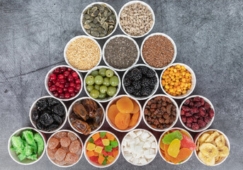 Obraz na płótnie Canvas Berries, seeds, dried fruits in round containers. Background with a mix of healthy snacks. Assorted vitamin food on a grey background.