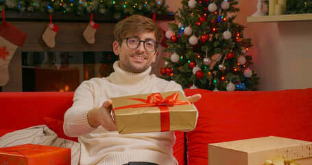 Obraz na płótnie Canvas Handsome man gives box gift to camera smiling. Give holiday Surprise Gifts Concept. Pozitive emotions on Christmas.