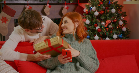 Emotional positive caucasian couple enjoying New Year. Christmas presents. Happy man is making christmas gift to his beloved woman. Shopping online gifts for Christmas