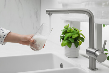 Woman filling glass with water from tap in kitchen, closeup