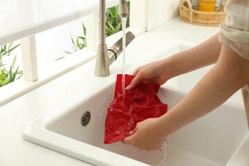 Woman washing beeswax food wrap under tap water in kitchen sink, closeup
