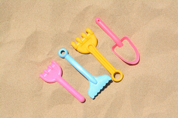 Fototapeta na wymiar Bright plastic rakes and shovel on sand, flat lay. Beach toys