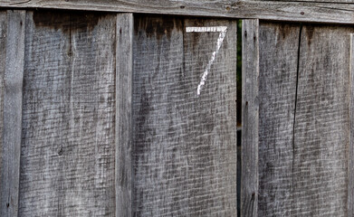 Fence made of rough old unpainted wooden boards with the number 7 painted on it. Vertical arrangement