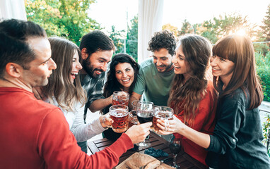 Group of happy young people having fun at the restaurant bar toasting with glasses of wine and beer together - Smiling friends at a terrace party at sunset - Youth and friendship concept