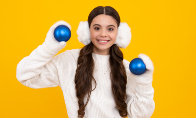 Fototapeta premium Portrait of teenager child girl wearing knitted gloves and winter sweater playing with christmas ball isolated on yellow studio background. Happy face, positive and smiling emotions.