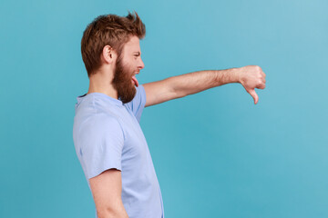 Side view of bearded man criticizing bad quality with thumbs down displeased grimace, showing...