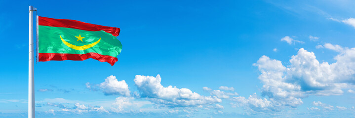 Obraz na płótnie Canvas Mauritania flag waving on a blue sky in beautiful clouds - Horizontal banner 