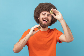 Portrait of funny laughing man with Afro hairstyle wearing orange T-shirt standing holding...