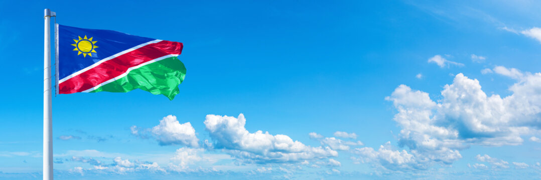 Namibia flag waving on a blue sky in beautiful clouds - Horizontal banner
