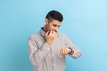 Portrait of impatient businessman pointing finger on his wrist watch with nervous face, time is...