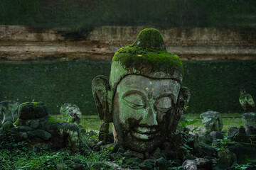 Ancient old ruin Head of Buddha statue carved from sandstone was destroyed and abandoned left in...