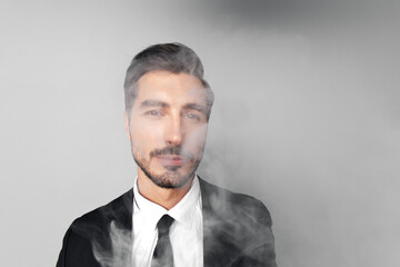 Man businessman in suit smokes e-cigarette and blows steam from his mouth, smoking and health stress in gray background close-up of face at wide camera angle