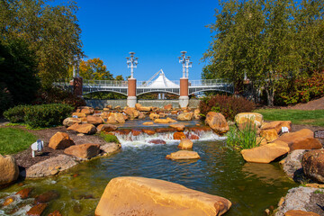 a gorgeous autumn landscape at World's Fair park with a flowing river with green water rushing over smooth brown rocks surrounded by autumn colored trees and lush green trees and grass in Knoxville - obrazy, fototapety, plakaty