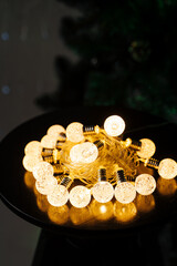 Warm yellow glowing christmas garland piled up on a dark table in an evening room with fur tree on background