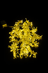 A pile of bright yellow christmas led lights on a black flat background, close up