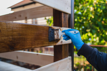 A close up of a paint brush painting a fence outdoors during the day