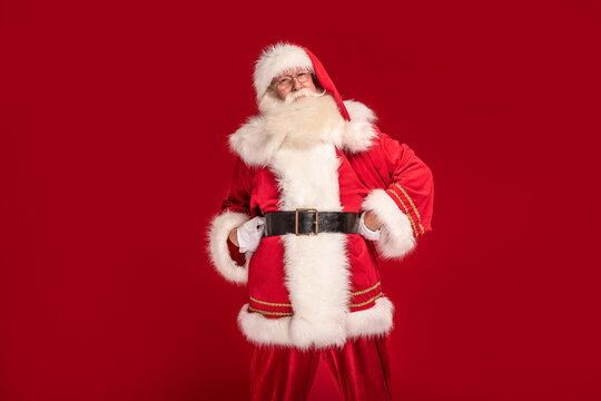 Happy bearded Santa Claus smiling to the camera, posing on red studio background. Merry Christmas and Happy New Year! A lot of copy space. Xmas sale