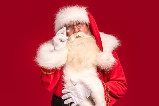 Portrait of bearded Santa Claus looking at the camera, posing on red studio background. Merry Christmas and Happy New Year! Xmas sale