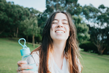 Portrait young woman greeting to camera holding a bottle of water for the dog, wide angle lens image