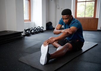 Young black man doing stretches on exercise mat at the gym