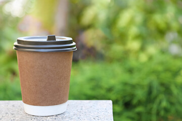 Disposable paper cup with plastic lid on stone parapet outdoors, space for text