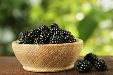 Bowl of fresh ripe blackberries on wooden table outdoors, closeup