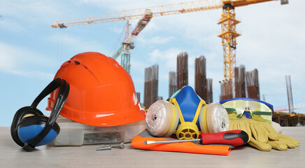 Safety equipment and tools on wooden surface and blurred view of construction site. Banner design