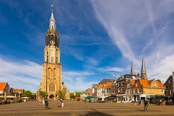 Fototapeten Scenic view of historical central Cameretten square of Dutch city of Delft with peculiar typical townhouses, busy street cafes and Gothic belfry of medieval Protestant church Nieuwe Kerk on summer day © JackF