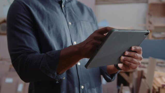 Close-up of young man scrolling on digital tablet while working in woodworking factory