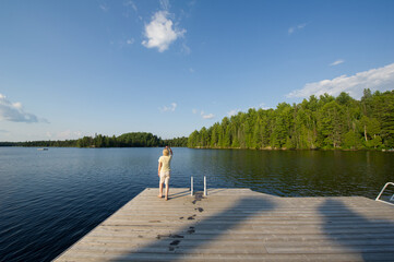 Young woman on a wooden dock admiring a lake in Algonquin Provincial Park, Muskoka Ontario Canada. The blue sky is showcasing beatiful fluffy clouds