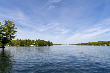 Lake view from a cottage dock in Muskoka, Ontario. Clouds are reflecting on the water while a canoe...