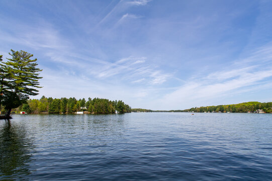 Lake view from a cottage dock in Muskoka, Ontario. Clouds are reflecting on the water while a canoe with inside two people is crossing the lake.
