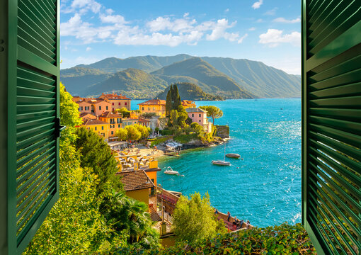 Fototapeta View through an open window with shutters looking down on the colorful picturesque village of Varenna, Italy, on the shores of Lake Como at summer.