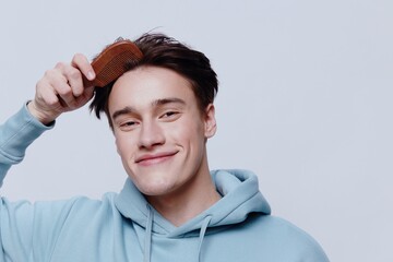Horizontal portrait photo .a pleasantly smiling young man in a light light blue hoodie, combs his...