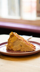 Trozo de torta de hojarasca, con interior de manjar y mermelada de frambuesa. Cubierto por una capa de crema merengue blanco. Sobre un plato de cerámica color morado
