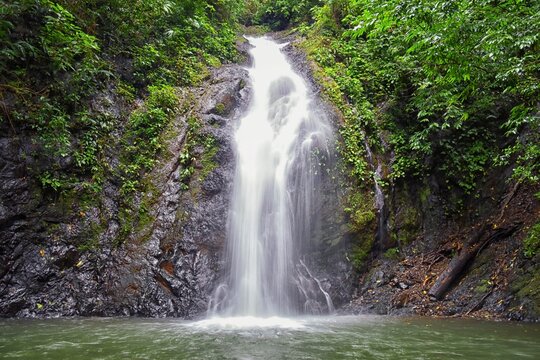Waterfall Jaco Costa Rica, Catarastas Valle Encantado - Hidden waterfall surrounded by green trees, vegetation, rocks, leaves floating on green and clear water. Central America.