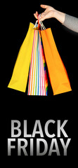Black Friday commercial event. Close-up of a woman's hand holding colorful shopping bags over black...