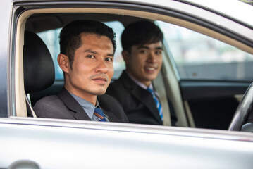 Two business men are driving and looking out of the car window.