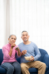 Happy smiling asian senior couple sitting on sofa and watching TV at home in living room. senior spending weekend time together.
