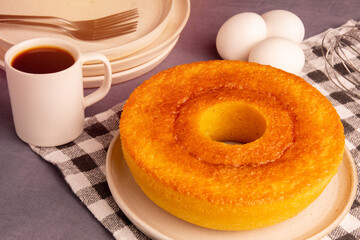 Homemade Redondo Pamonha Cake (Fuba Cake), made from corn, with a coffee and eggs in the background, on a checkered picnic tablecloth