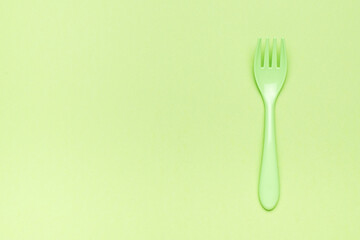 Plastic green fork on a green background. A place for your text. Flat lay.