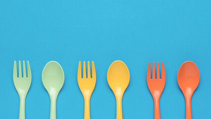 Orange, yellow and green plastic forks and spoons on a blue background. Minimal concept of plastic...
