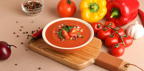 Bowl with tasty gazpacho and vegetables on beige background