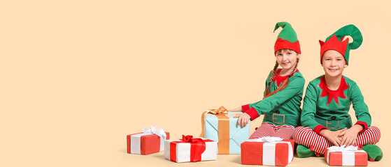 Little children in costumes of elves and with gifts on beige background with space for text