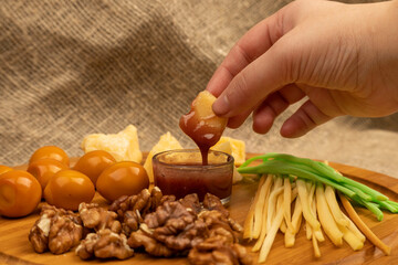 Someone dips a piece of cheese in honey against a background of assorted different varieties of cheese.