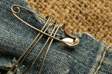 Safety pins on a strip of denim against a homespun fabric with a rough texture.
