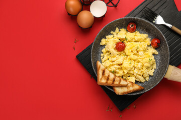 Frying pan with tasty scrambled eggs, tomatoes and toasts on red background