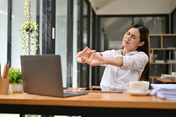 Uncomfortable Asian businesswoman stretching her arms, suffering from office syndrome.